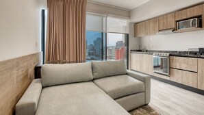 A modern apartment with a sectional sofa, a kitchen with a microwave and stove, and a large window with curtains. - MYLA Premium Loft in Chapultepec HighF (Mexico City)