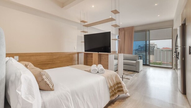 A modern hotel room with a large bed, a flat-screen TV, a sofa, and a balcony with a city view. - MYLA Premium Loft in Chapultepec HighF (Mexico City)