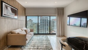 A modern living room with a sofa, a dining table, and a large window offering a city view.