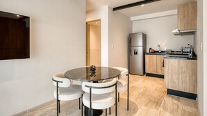 A modern kitchen with a built-in refrigerator, a dining area with a marble table and cushioned chairs, and a wooden cabinet.