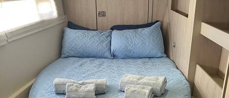 A compact bed with a quilted blue mattress, two pillows, and two folded towels.