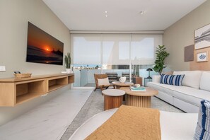 A modern living room with a large window, a sofa, a coffee table, and a TV mounted on the wall.