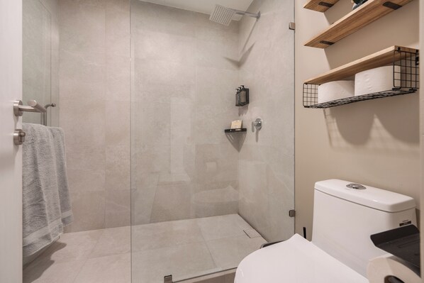 A modern bathroom with a glass-enclosed shower, a toilet, and wooden shelves with toiletries.