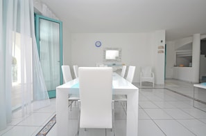 Une pièce moderne et bien éclairée, avec une table et des chaises, un grand miroir et une vue sur l’extérieur grâce à une porte vitrée.