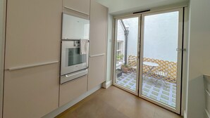 A kitchen with a built-in oven and microwave, a sliding glass door leading to a patio with a wooden lattice table and chairs. - Boutique Townhouse in Fitzrovia | Pass the Keys (London)