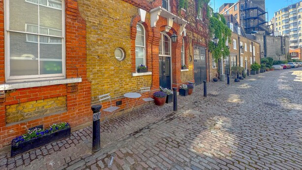A cobblestone street lined with red brick buildings, some with windows and doors, and a few with plants. - Boutique Townhouse in Fitzrovia | Pass the Keys (London)