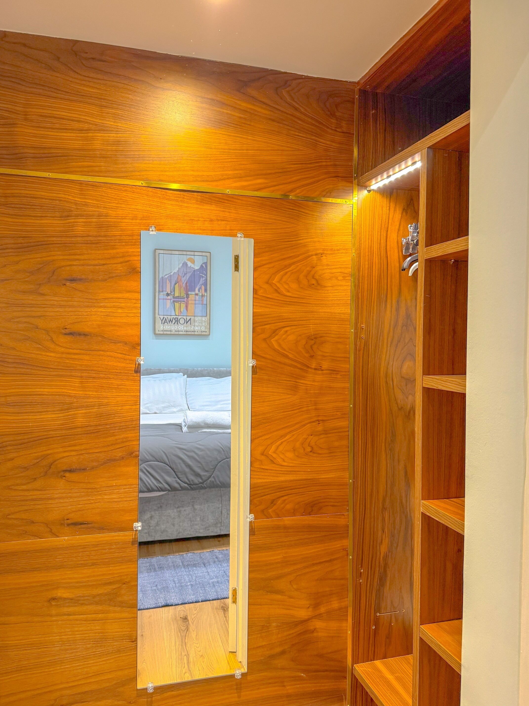 A wooden-paneled room with a mirrored wardrobe, a bed with gray bedding, and a framed picture on the wall.