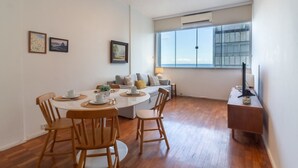 A modern living room with a dining area, featuring a sofa set, a coffee table, and a TV on a wooden stand.