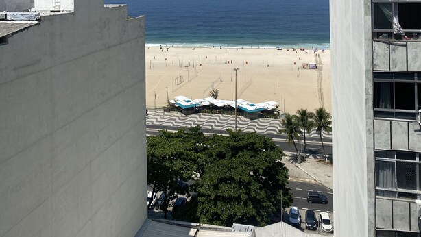A beach view from a high-rise building with a clear sky, a sandy beach, and a few umbrellas.