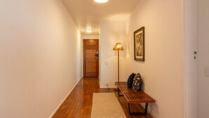 A hallway with wooden flooring, a bench, a lamp, and a door at the end.