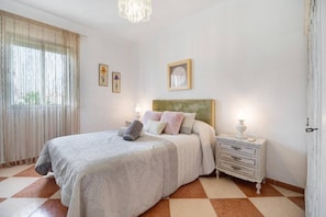 A bedroom with a bed, nightstands, a chandelier, and artwork on the walls.