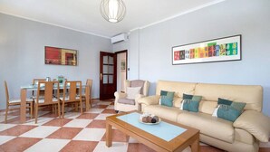 A living room with a beige sofa, a dining table with chairs, a coffee table, and a wall-mounted air conditioner. - Grand Beachside Apartment (Cádiz)