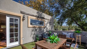 Un patio al aire libre con mesa y sillas de madera, un banco incorporado y una puerta corrediza de vidrio que da a un espacio interior.
