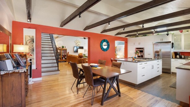 Una cocina amplia con gabinetes blancos, un refrigerador de acero inoxidable y un comedor con mesa y sillas de madera.