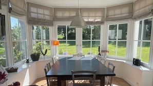 A dining area with a large table, chairs, and a view of a garden through large windows.