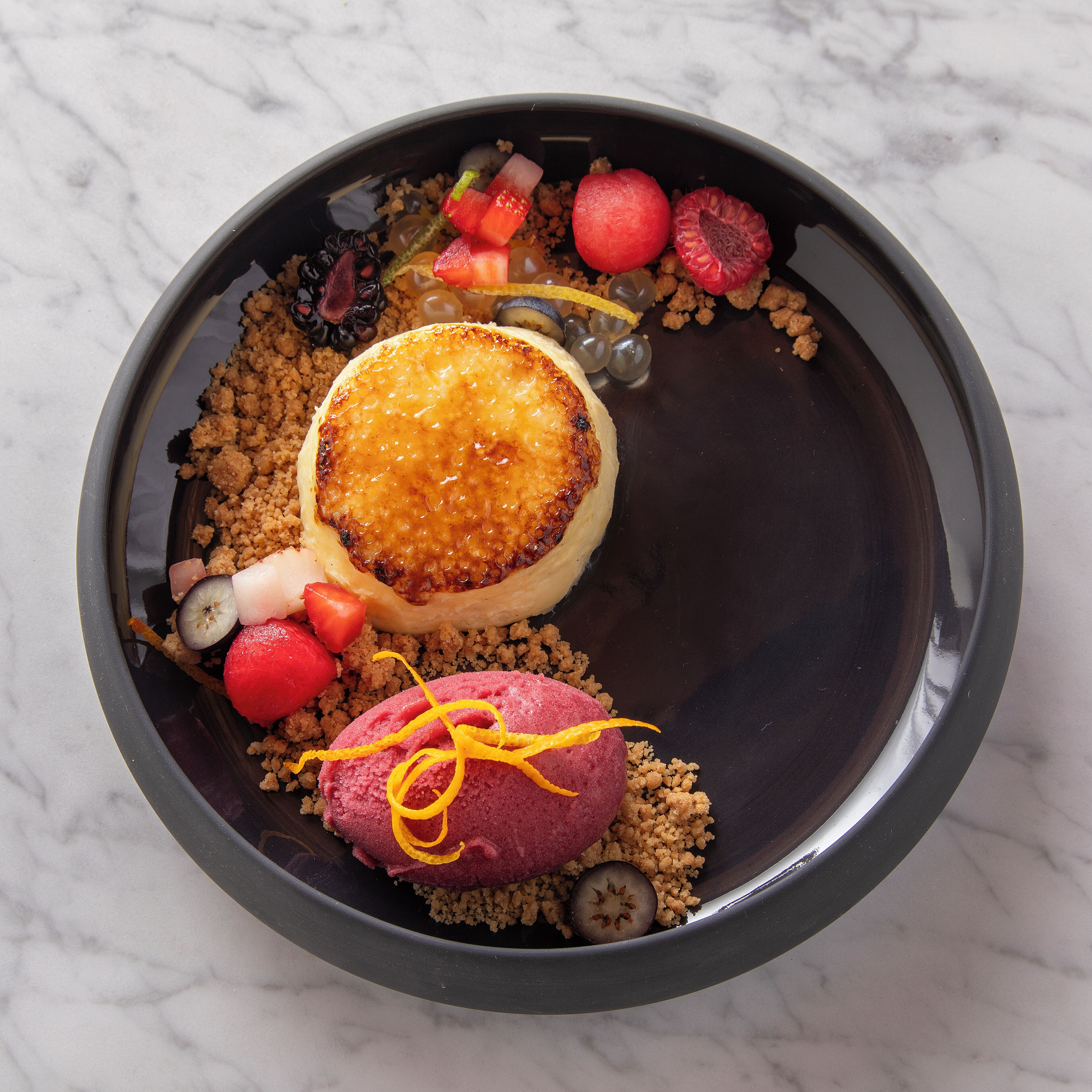 A dessert plate with a caramelized top, garnished with fruit and a decorative orange peel.
