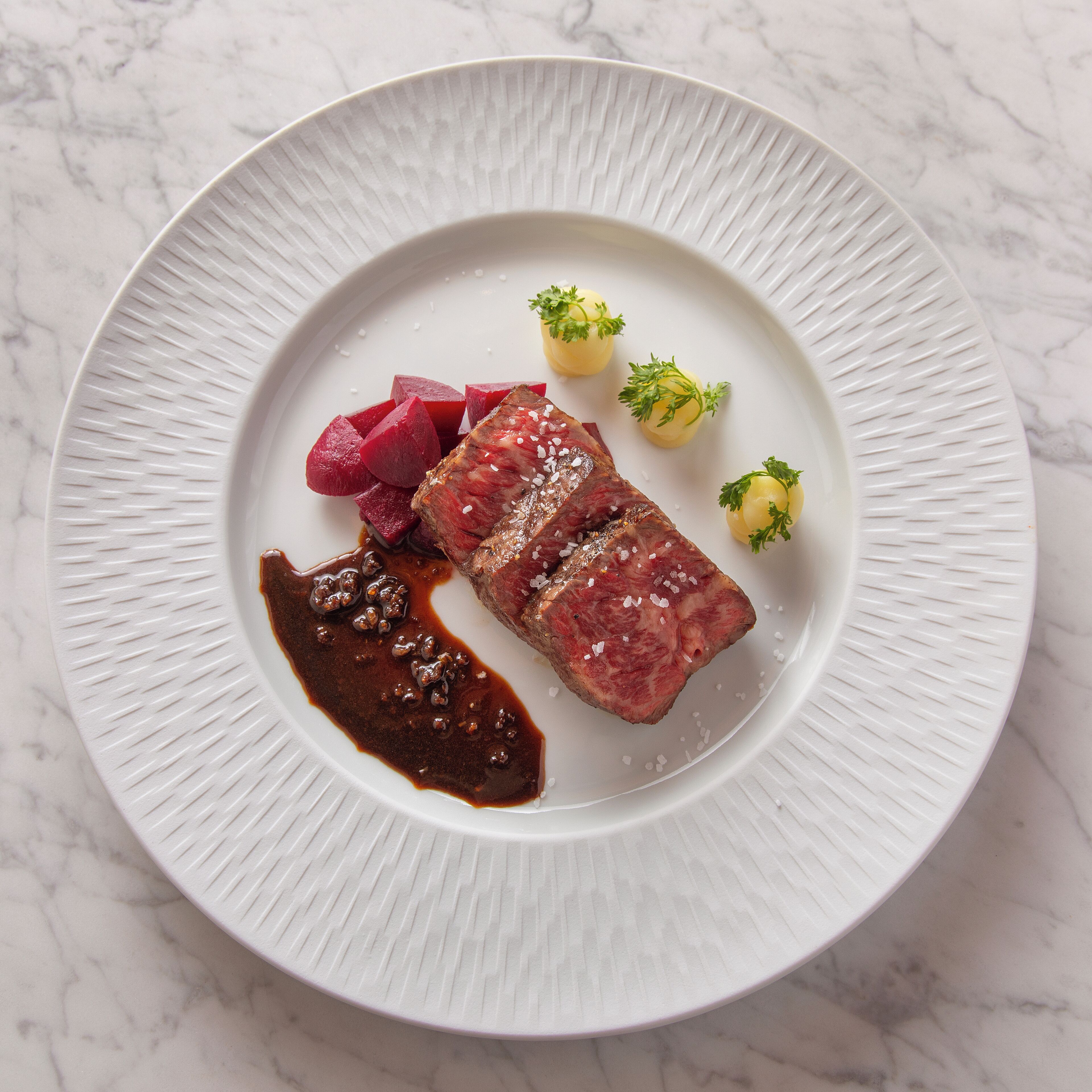 Une assiette blanche contenant un steak, des betteraves et une sauce.