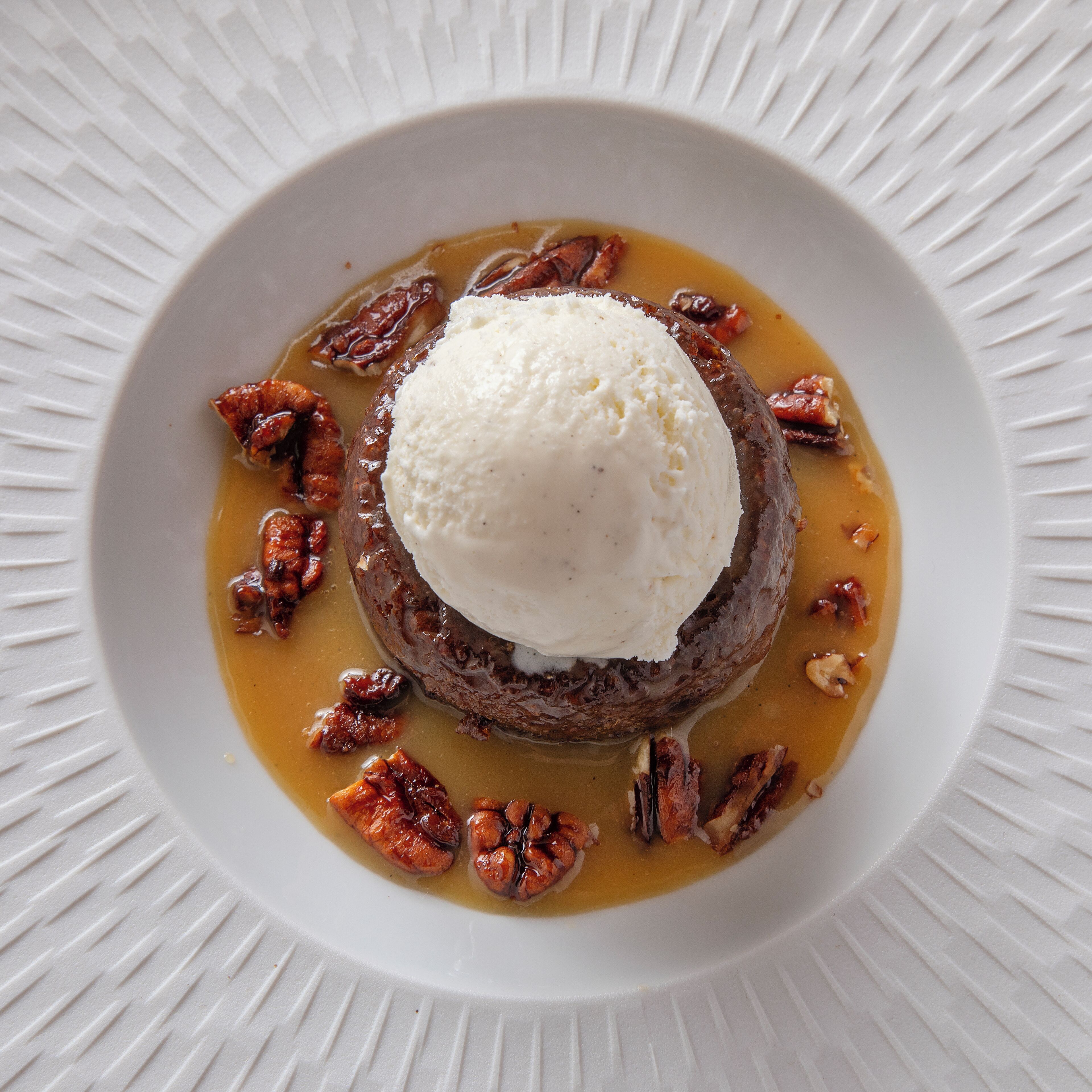A dessert with a scoop of ice cream on top, surrounded by pecans, on a white plate.