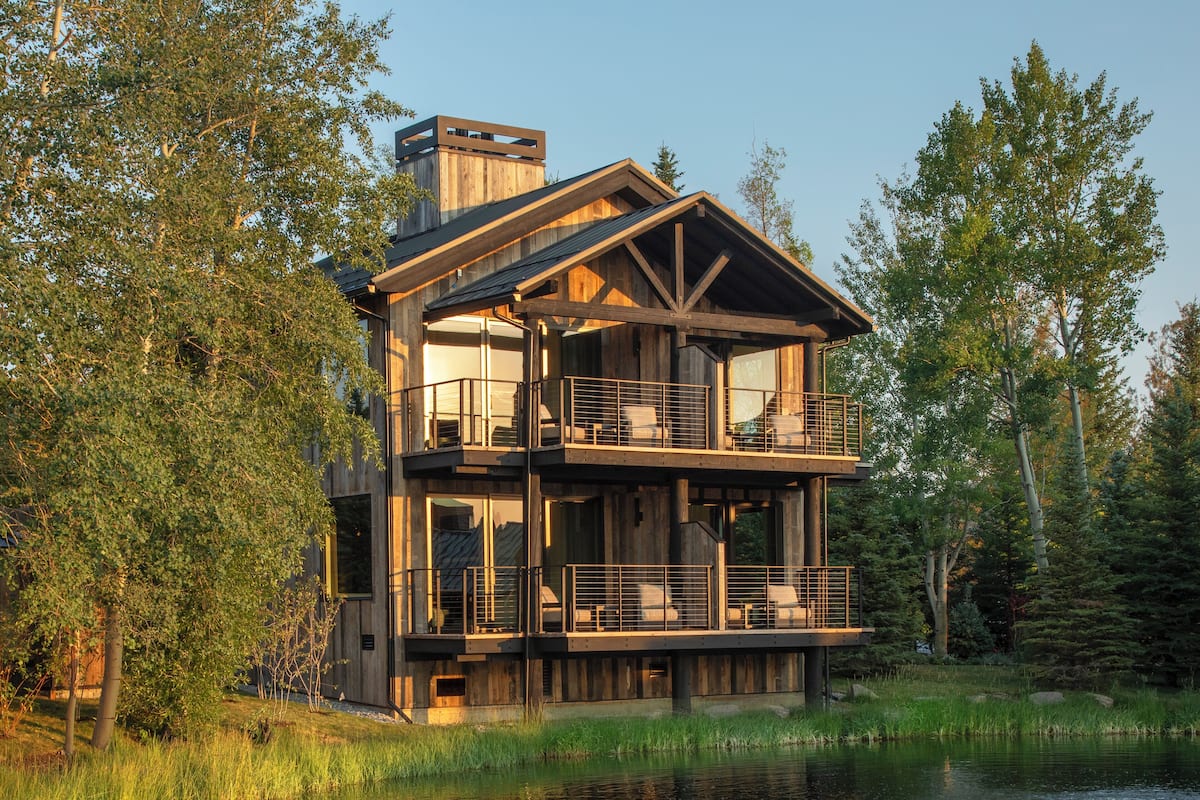 A multi-story wooden cabin with balconies overlooking a lake, surrounded by trees.