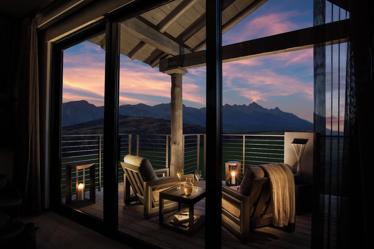 A balcony with a view of mountains and a sunset. There are two chairs and a table with a candle.