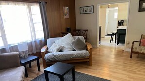 Una sala de estar acogedora con un sofá, una mesa de centro y una alfombra. Se observa un comedor con sillas y una mesa. Se distingue una cocina al fondo.