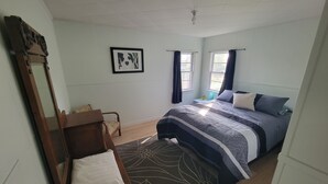 Un dormitorio con cama, un banco de madera, un espejo, un cuadro enmarco y una ventana con cortinas.