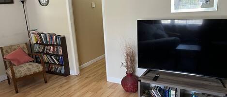 A living room with a flat-screen TV, a bookshelf, a chair, a red vase, and a framed picture on the wall.