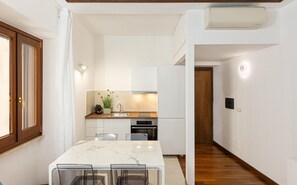 A modern kitchen with white cabinets, a built-in oven, and a white refrigerator. There is a dining table with chairs in the foreground. - Vicolo Trevi apartment (Rome)