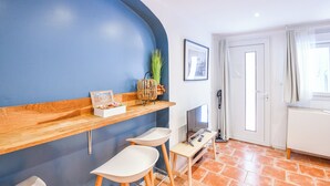 A modern room with a blue accent wall, a wooden counter, two white bar stools, a TV, and a door with curtains.