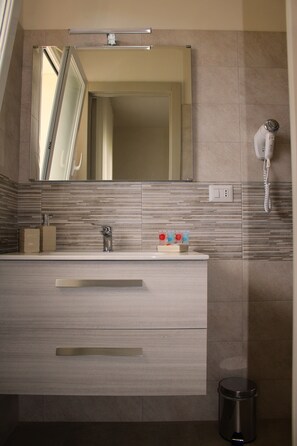 A modern bathroom with a large mirror, a sink with a faucet, a trash bin, and a hairdryer on the wall. - La Bella Dimora (Otranto)