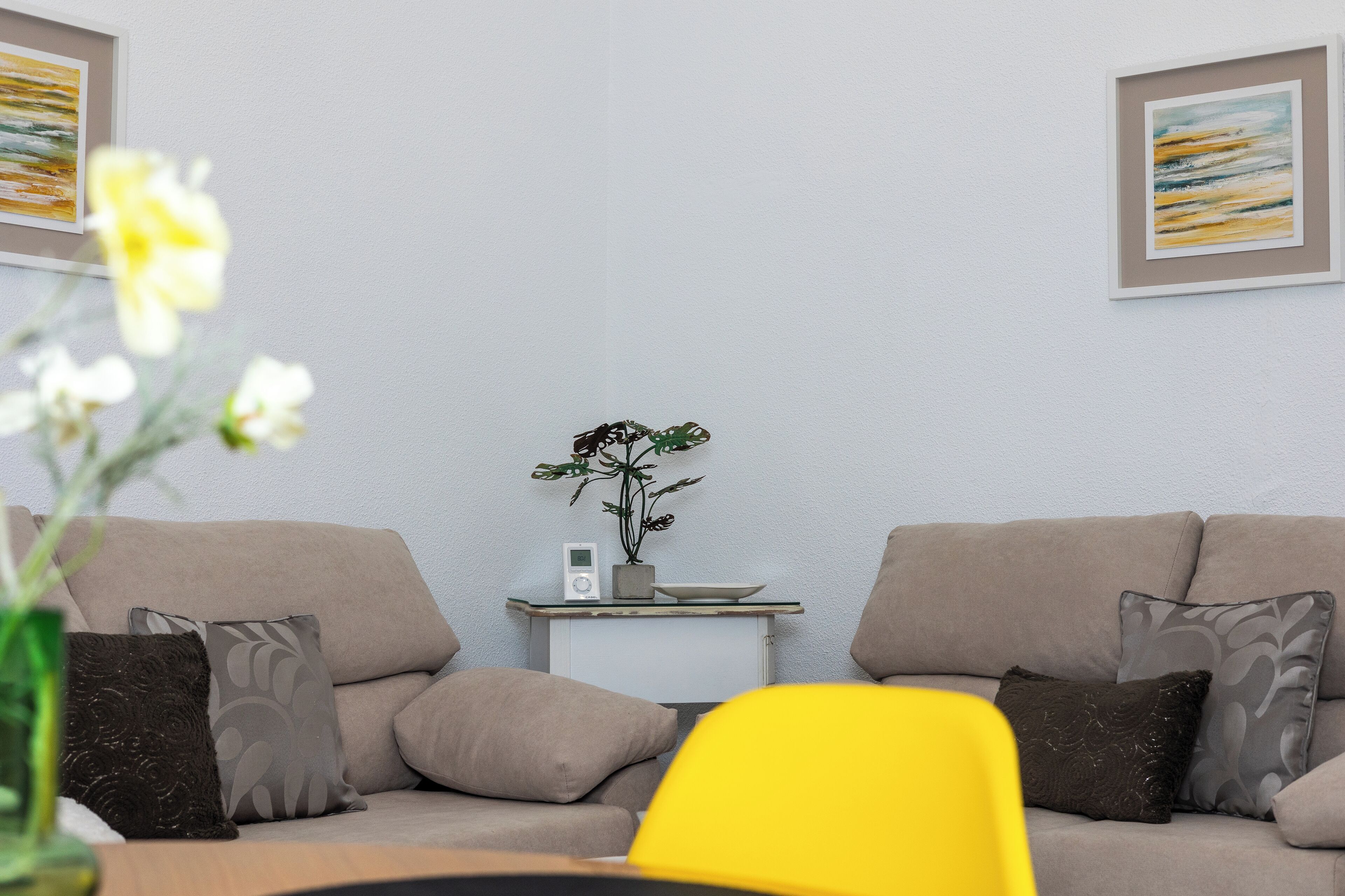 Una sala de estar con un sofá color crema, una mesita auxiliar con una planta y un sillón amarillo.