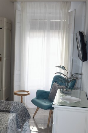 A bedroom with a bed, a blue armchair, a small round table, a white cabinet, and a potted plant. - Alojamiento El Carmen by La Condesa Carmen (Manzanares)