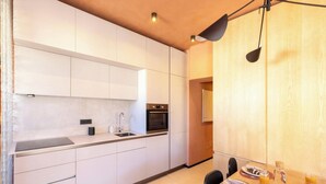 Une cuisine moderne avec des armoires blanches, un four encastré et un coin repas comprenant une table et des chaises en bois.