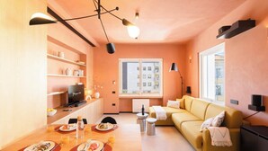 Un salon moderne avec un canapé jaune, un coin repas avec une table mise pour le petit-déjeuner et une grande fenêtre offrant une vue sur la ville.
