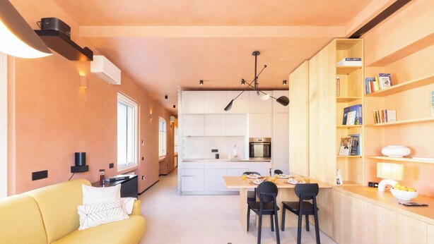Une cuisine moderne avec des meubles blancs, un coin repas doté d’un canapé jaune et une bibliothèque remplie de livres.