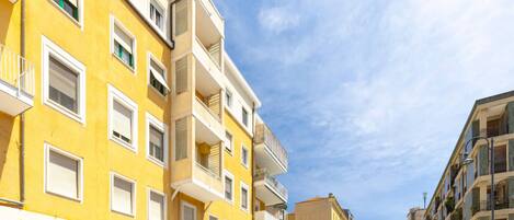 A street lined with multi-story yellow buildings, parked cars, and a clear blue sky.