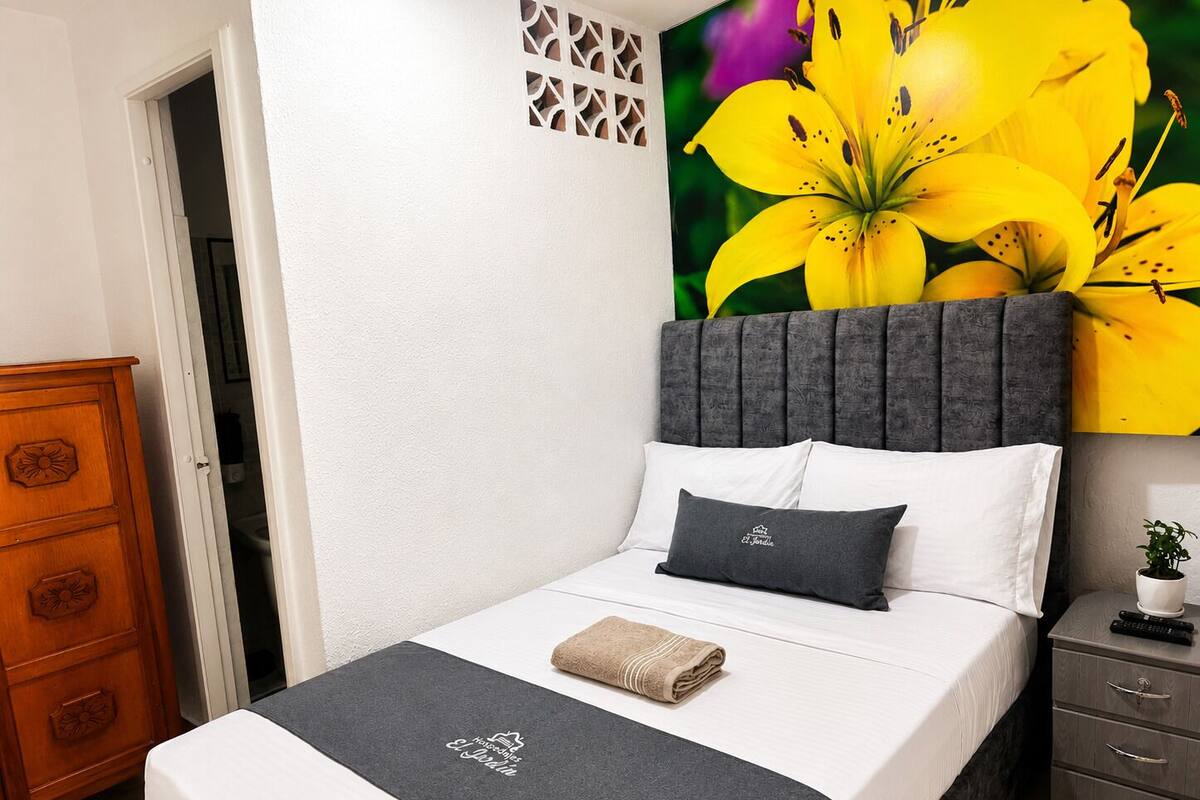 Une chambre à coucher comprenant un lit, une table de chevet, une commode et une grande œuvre d’art à motifs floraux accrochée au mur.