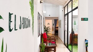 A hallway with a sign reading 'EL JARDIN,' a wooden table with chairs, a red chair, and a blue sofa. - Hospedajes El Jardin (Envigado)