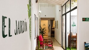 A hallway with a sign reading 'EL JARDÍN,' a seating area with a table and chairs, and a view through a glass door to an outdoor area. - Hospedajes El Jardin (Envigado)