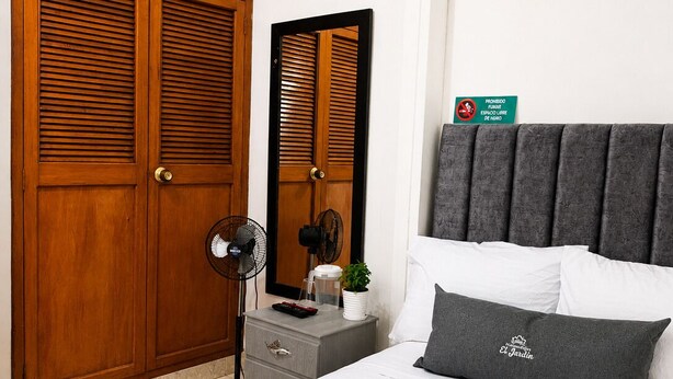 A bedroom with a bed, a bedside table, a mirror, a wardrobe, and a sign indicating no smoking. - Hospedajes El Jardin (Envigado)