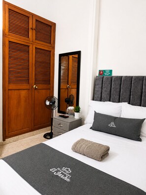 Een slaapkamer met een bed, nachtkastje, spiegel, kledingkast en een bordje met een rookverbod.
