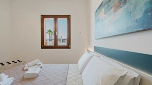 A hotel room with a bed, a window with a view, a painting on the wall, and a towel rack. - VILLA CON PISCINA (Balestrate)