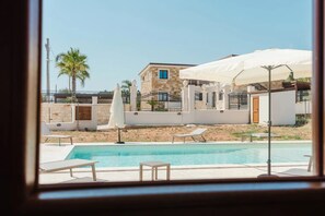 A pool area with lounge chairs and umbrellas, a stone building, and a fenced property. - VILLA CON PISCINA (Balestrate)