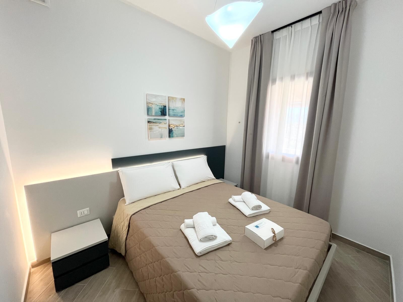 Una camera d'albergo moderna con un letto, un comodino, una lampada a parete e una finestra con tende.