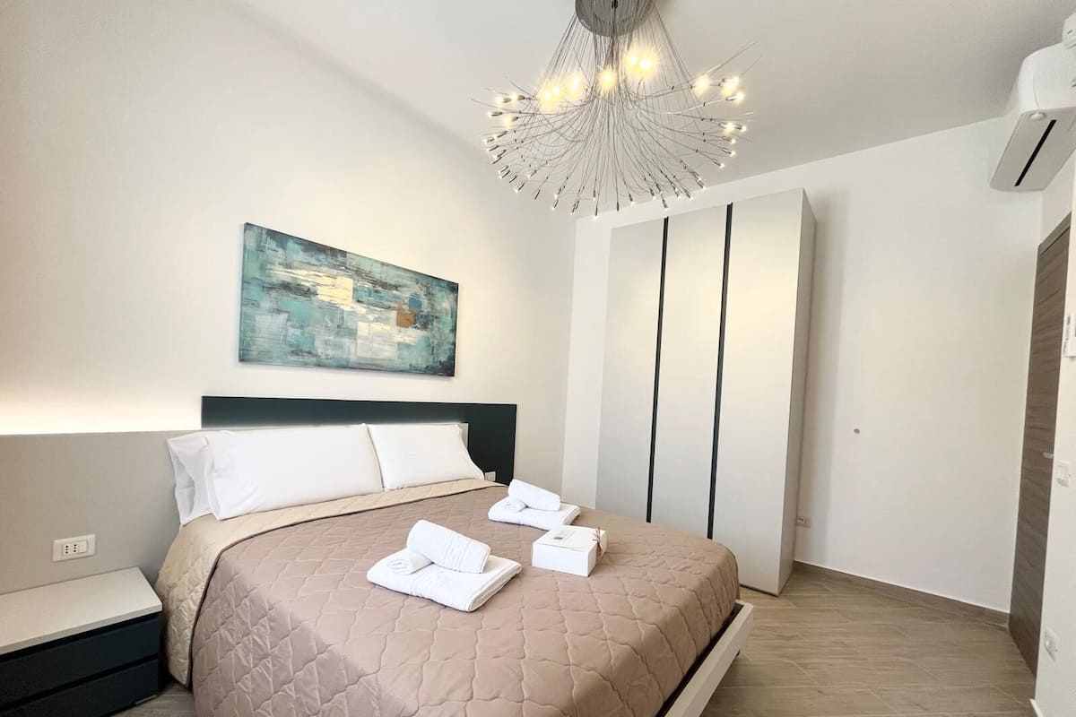 Une chambre moderne avec un lit, un tableau, un lustre original et une armoire.