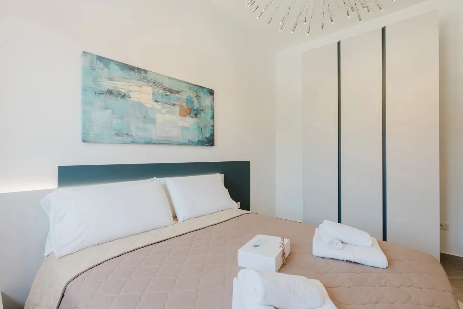 Ein modernes Hotelzimmer mit einem großen Bett, einem Kopfteil, einem Bild an der Wand und einem Kleiderschrank.