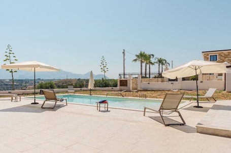 Una piscina al aire libre, sombrillas, sillones reclinables de piscina