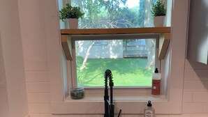 Una cucina con un lavello nero, una finestra che si affaccia su un cortile interno e uno scaffale con due piante in vaso.