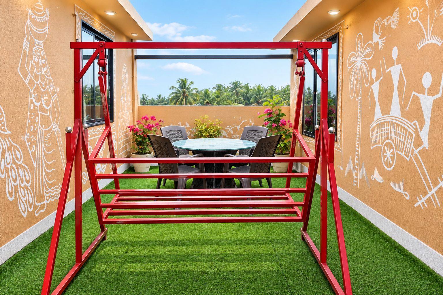 A red swing set in a room with a green artificial turf floor, a round table with chairs, and a view of palm trees through a glass door.