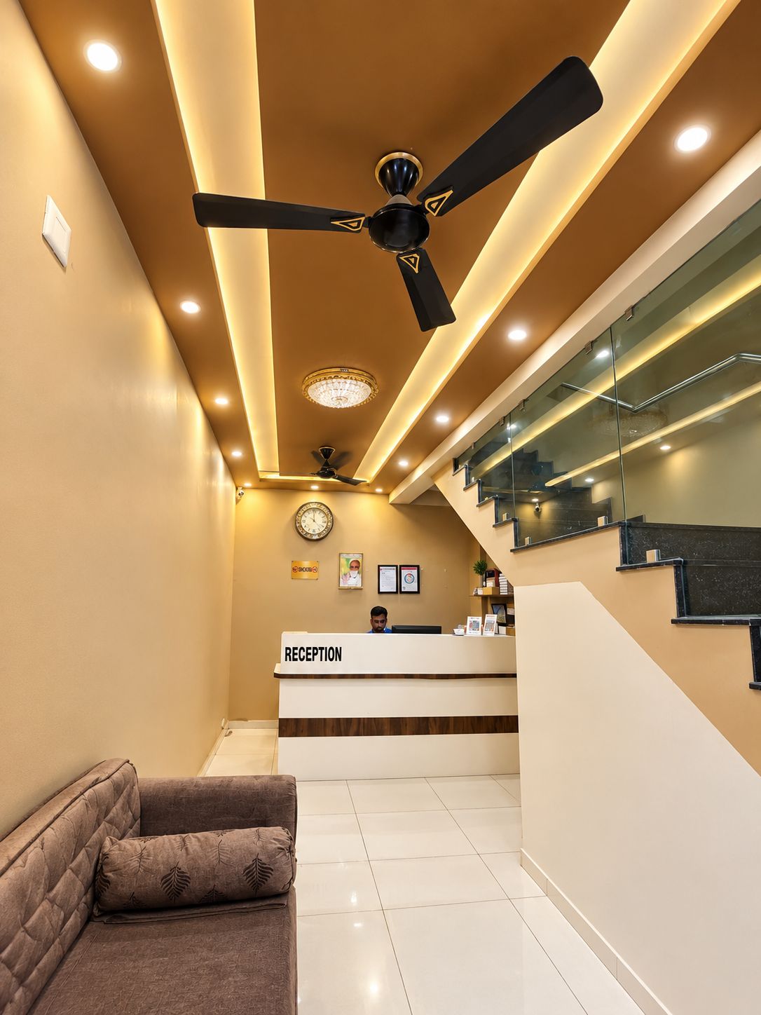 Un área de recepción con mostrador, ventilador de techo, reloj y escalera.
